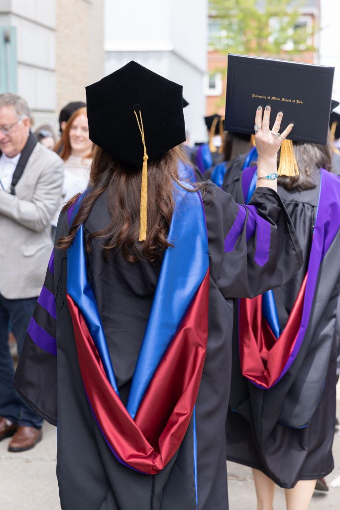 Photo of a student from the back wearing robs and tam holding up her degree. 