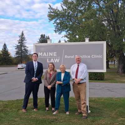 A photo of four individuals standing in front of a sign that reads "Rural Practice Clinic.