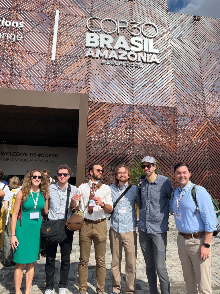 Photo of Stephanie Forbes, JD Candidate; Thacher Carter, JD Candidate; Samuel Walter, PhD Candidate in Earth Science; Keiran Lorentzen, JD Candidate; Professor Anthony Moffa, Associate Dean for Innovation; Adam Fortier-Brown, JD Candidate standing in front of a sign that says Brazil.