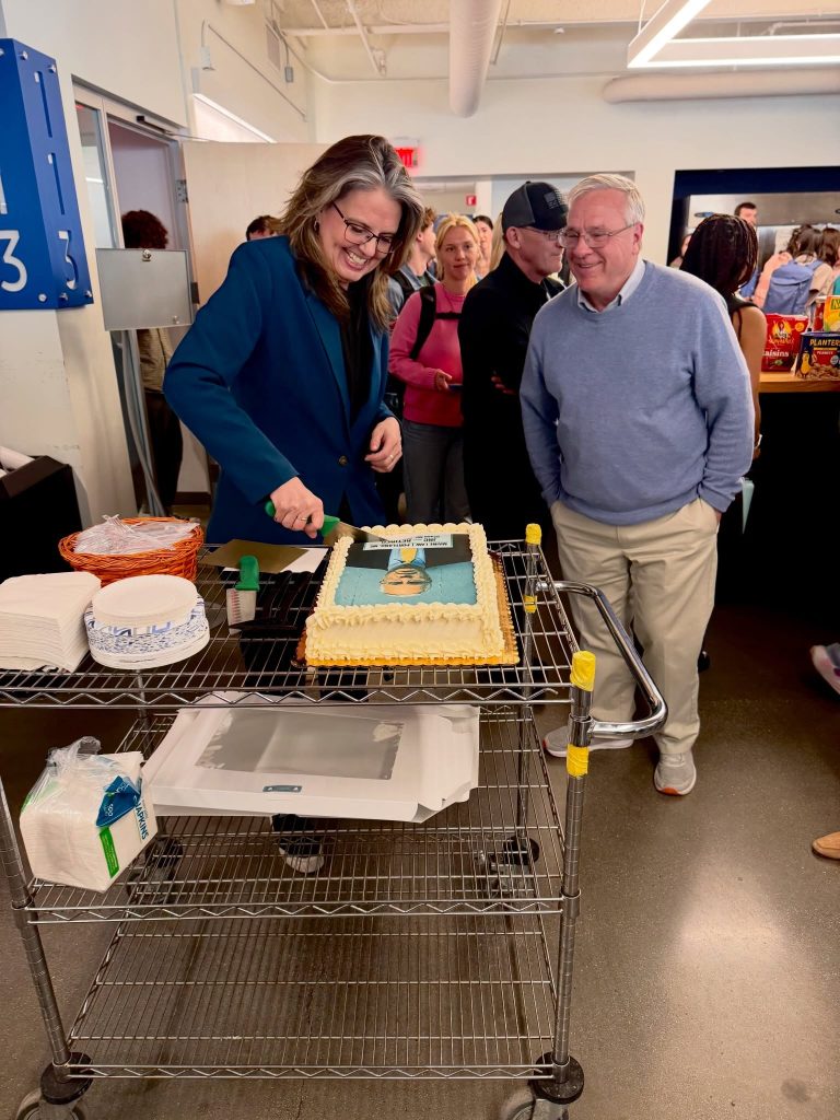 Photo of Chapman standing next to a woman cutting a cake with his face on it.