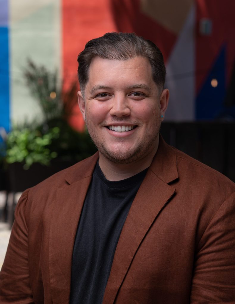 Portrait of Rivera smiling in front of greenery 