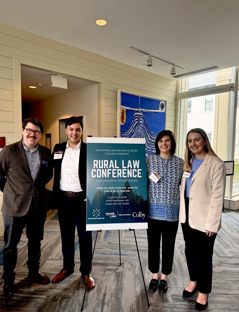 Photo of 4 students standing next to a sign that says Rural Law Symposium