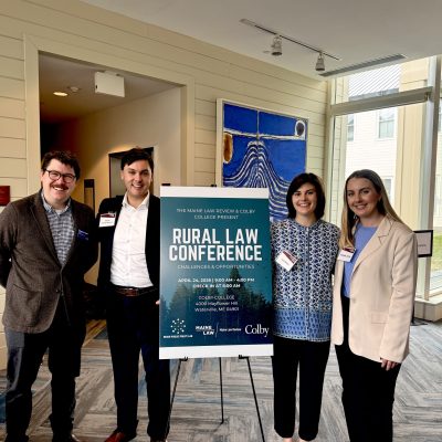 Photo of 4 students standing next to a sign that says Rural Law Symposium
