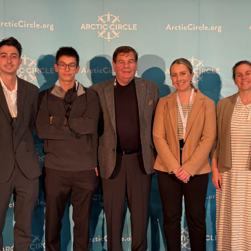 Photo of four students standing with Professor Norchi in front of a sign that says "Arctic Circle."