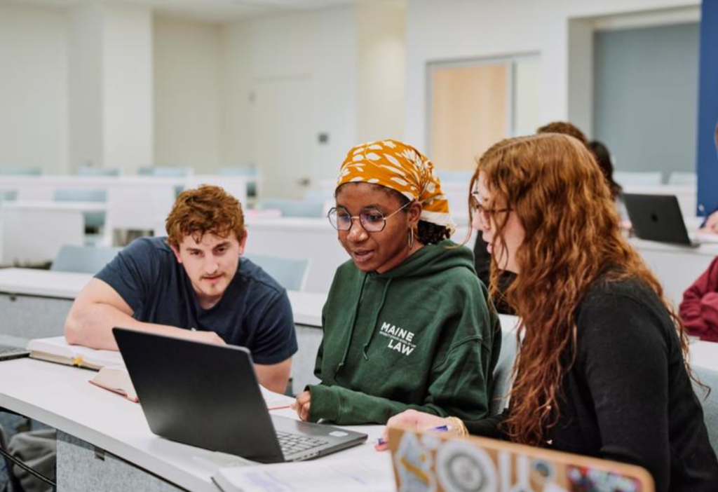 Photo of three Maine Law students huddled around a computer in a classroom