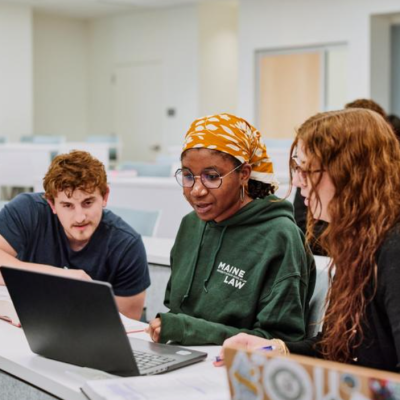 Photo of three Maine Law students huddled around a computer in a classroom