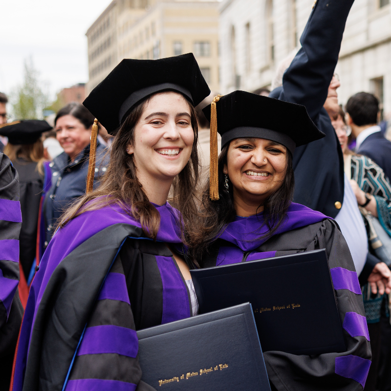 Photo of two women posing and smiling in graduation regalia.