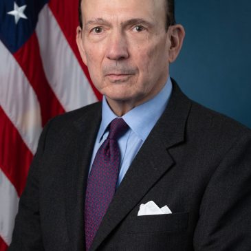 Photo of man in a suite in front of a U.S. flag.
