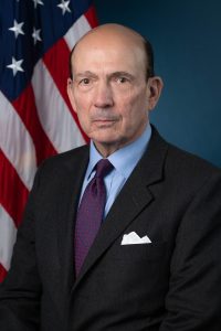 Photo of man in a suite in front of a U.S. flag.